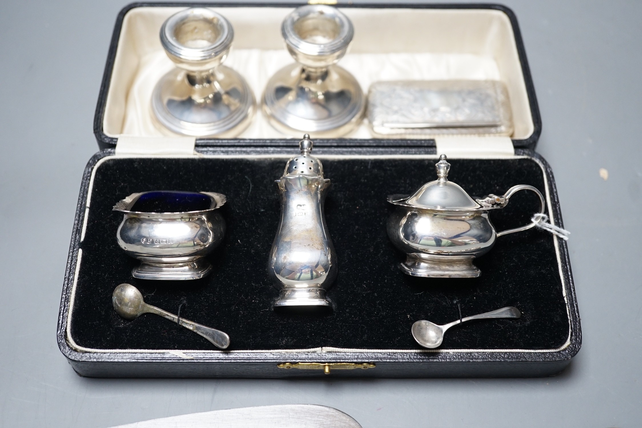 A cased George V silver three piece condiment set, Birmingham, 1930, a Victorian engraved silver snuff box, a pair of silver mounted dwarf candlesticks and a silver handled cake slice.